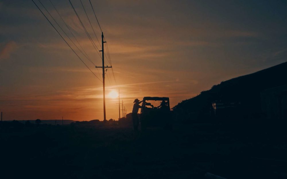 The cowboy Derek Kolbaba leaning on his truck in front of a power line and beautiful sunset.