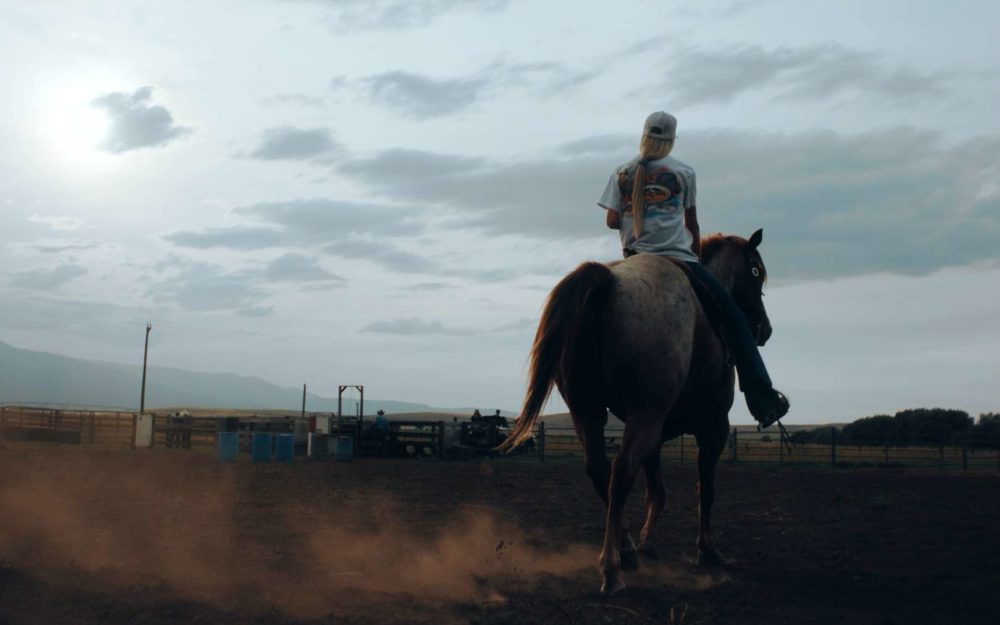 A girl riding a horse in front of a sunset in a dusty field on a dry day with dust flying through the air.