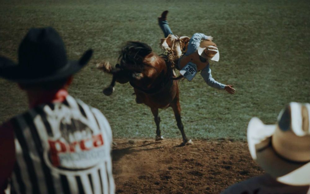 A cowboy falling down from a horse while riding in a rodeo competition in front of two other cowboys.