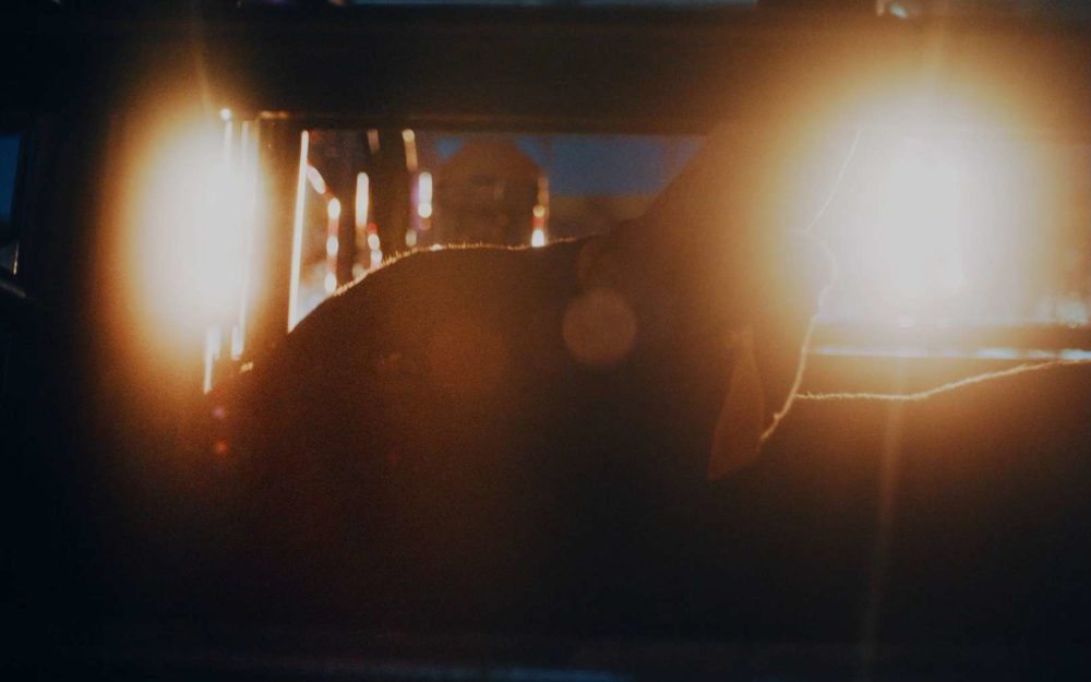 A bull in a cage in front of lights, looking towards the camera at night before a rodeo turnament.