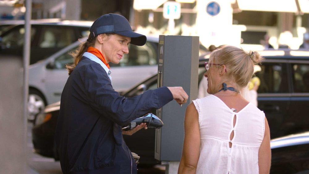 The main actress of the Twint commercial giving money to a woman in front of cars in the city of zurich