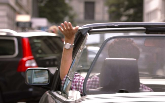 A person waving out of a car while driving through the city of zurich for the commercial for Twint.