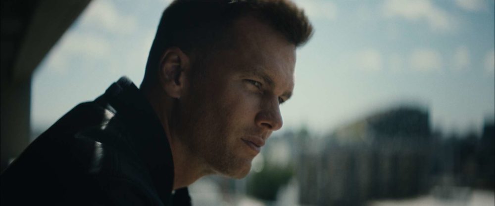 The famous football player Tom Brady looking in the distance on a sunny day.