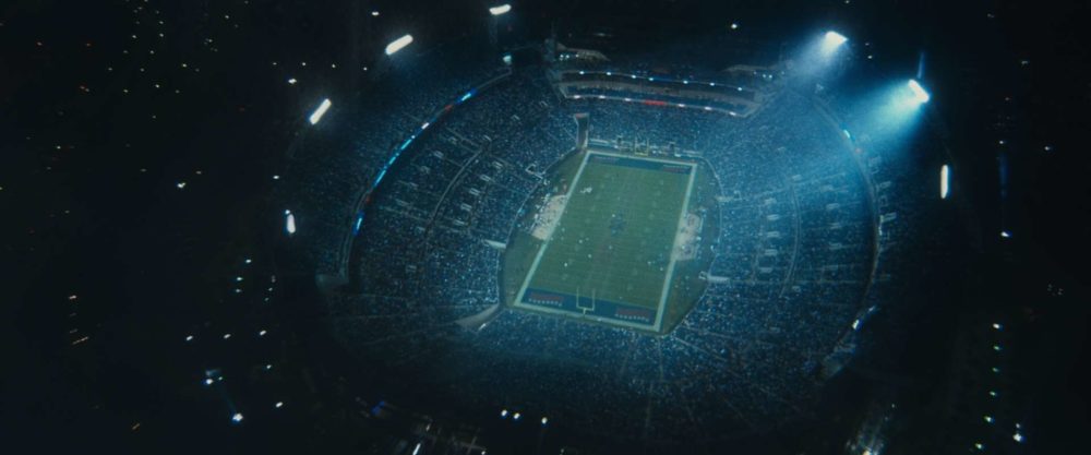 A big stadium in pouring rain from above. The floodlights are turned on.