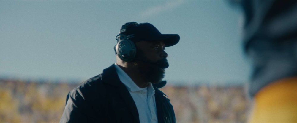 A football coach with some headphones cheering for his players in a stadium.
