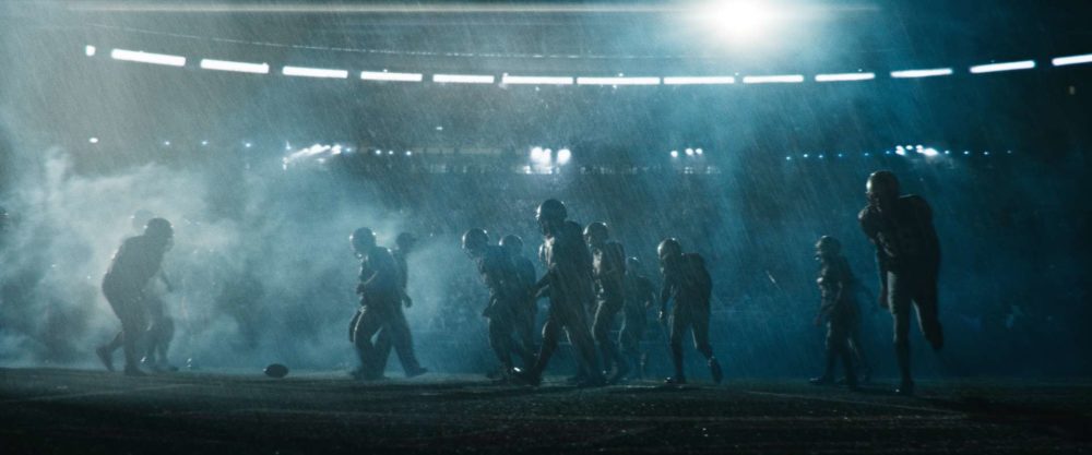 A lot of football players in pouring rain gathering around the ball in a stadium.