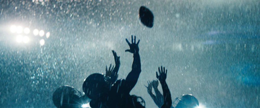 Four football players jumping towards the ball in pouring rain in a stadium.
