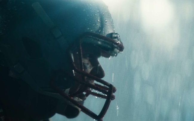 The football player Tom Brady screaming in the rain waring a helmet