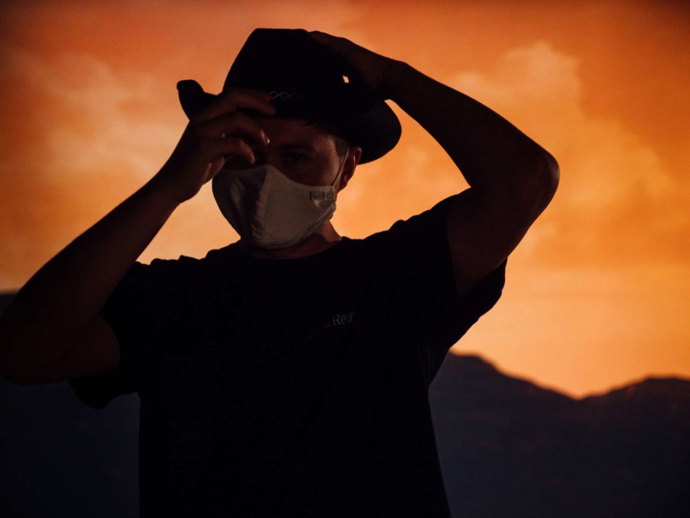 A person wearing a cowboy hat in front of a sunset in a canyon.