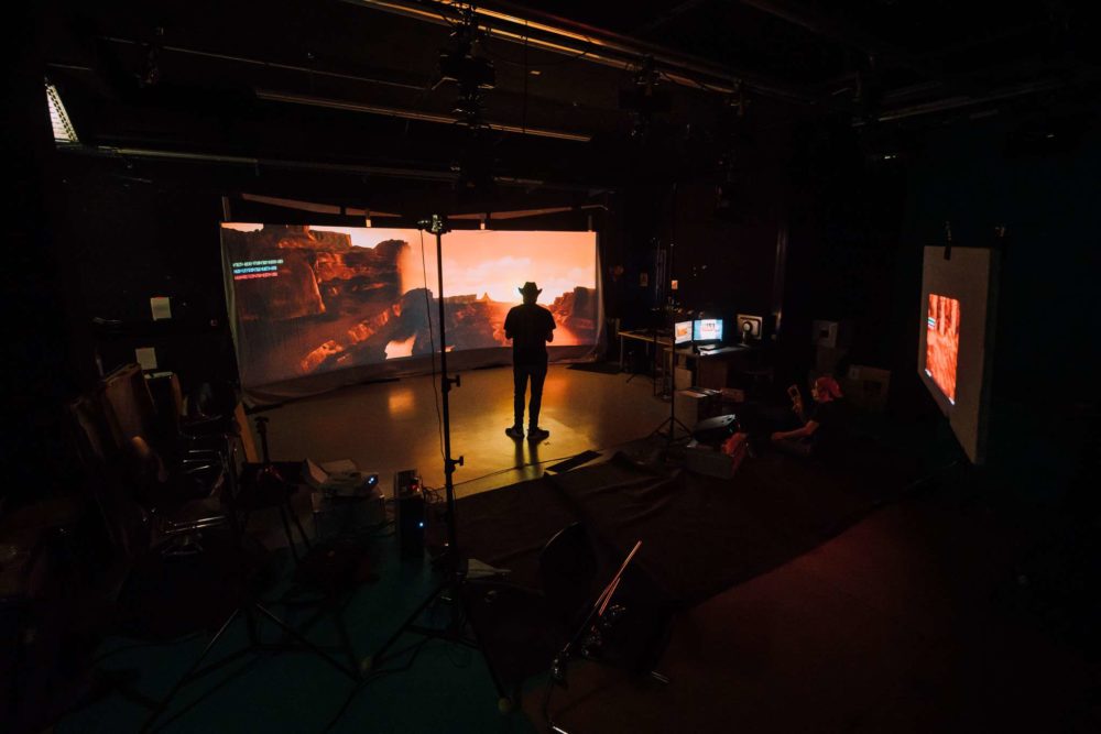 A person with a cowboy hat standing in front of a virtual production setup.