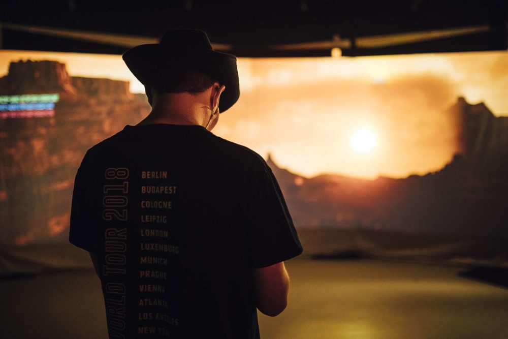 A person with a cowboy hat standing in front of a virtual production setup.