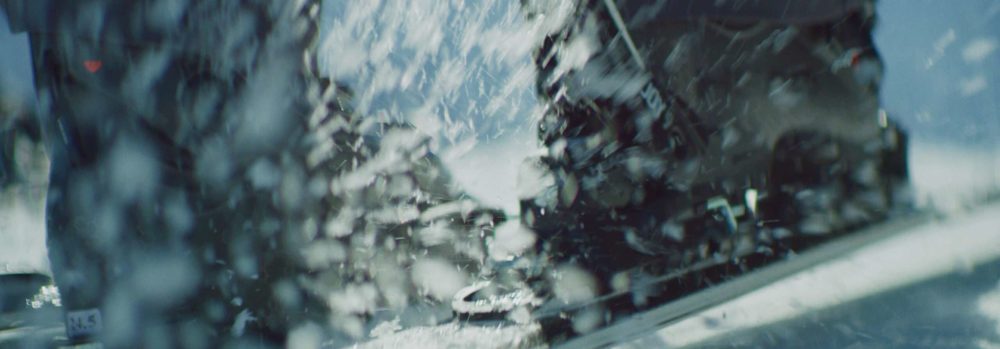 A skier putting on his skies and the snow is flying all around.