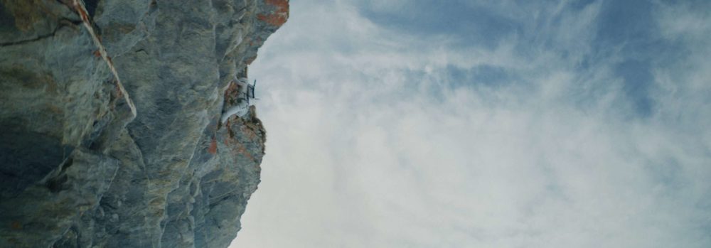 A climber in the middle of a steep wall climbing up towards the sky.