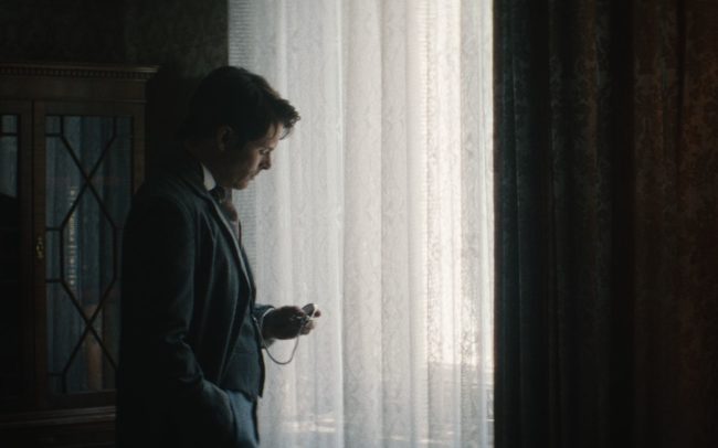 James Marsden playing F.A. Jones, looking at a IWC watch in front of a big window.
