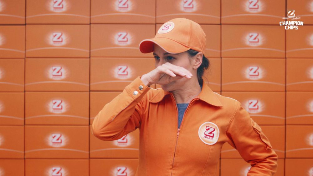 A woman in an orange suit standing in front of a wall made of orange boxes.