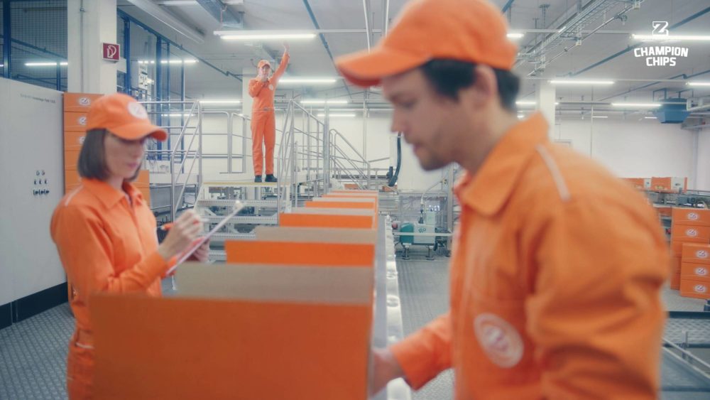 Two persons packing orange boxes, while being whatched by a woman.