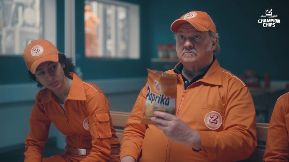 An man in an orange suit holding a pack of chips